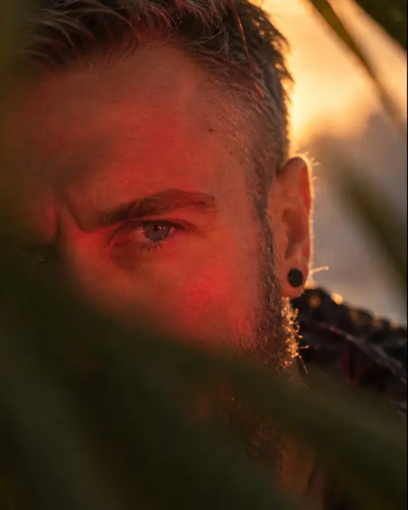 Close-up of a man's eye catching red light, soft green palm blur covering the lower half of the frame