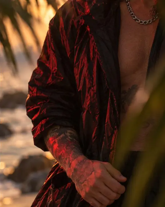 Detail of a black crinkled nylon parka edge with a red flash highlight and a gold rim of sunset
