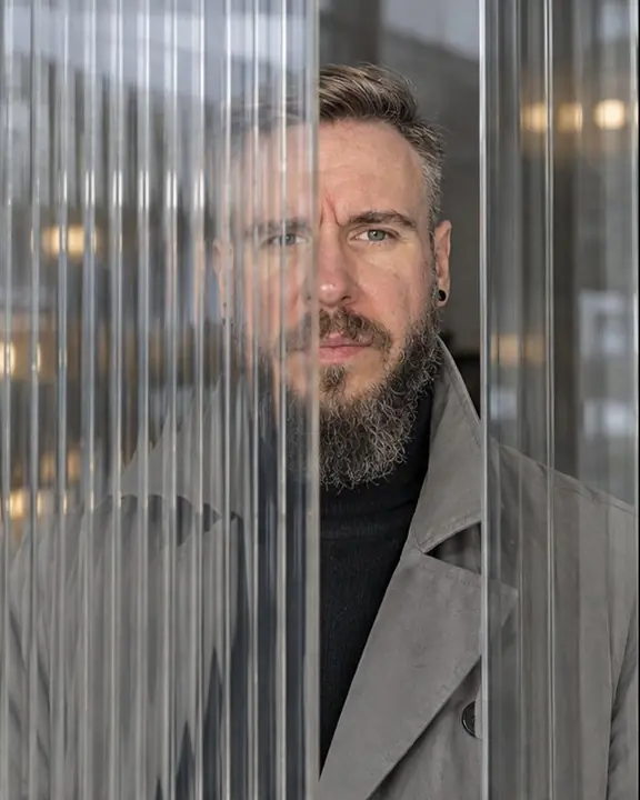 A bearded man seen through reeded glass, face clear in a smooth vertical strip, his body broken into thin slices