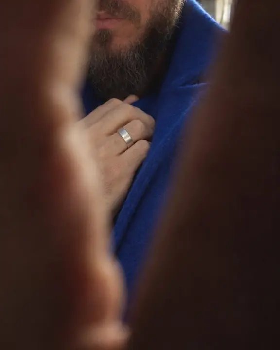 Seen through a gap between two hands, a fragment of a cobalt coat and a silver ring catch the light