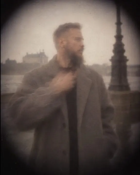 A stone-gray coat sleeve, soft and slightly doubled, in faded pinhole film color with a dark vignette