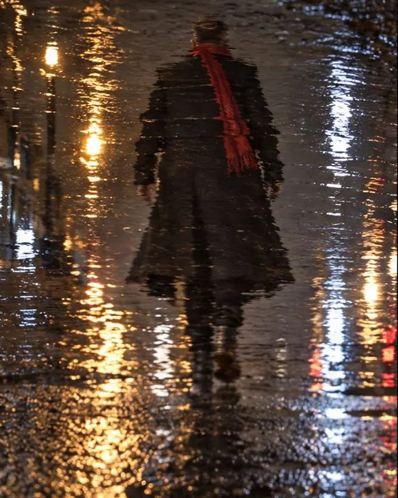 Reflection of a man walking away in a puddle, stretched by ripples, the real figure out of frame