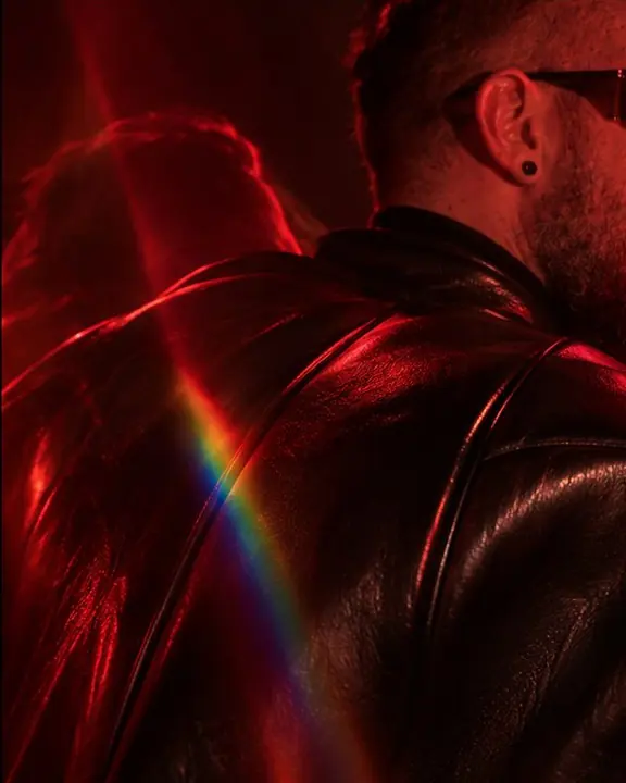 Detail of a padded leather shoulder seam doubled by a prism in red light, crossed by a thin sliver of spectrum