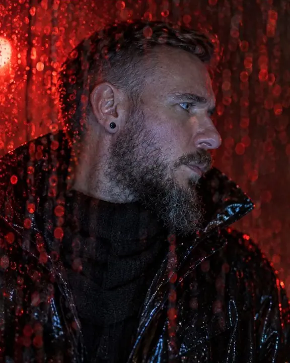 Profile of a bearded man looking away behind a wet window, red raindrops sliding across his face