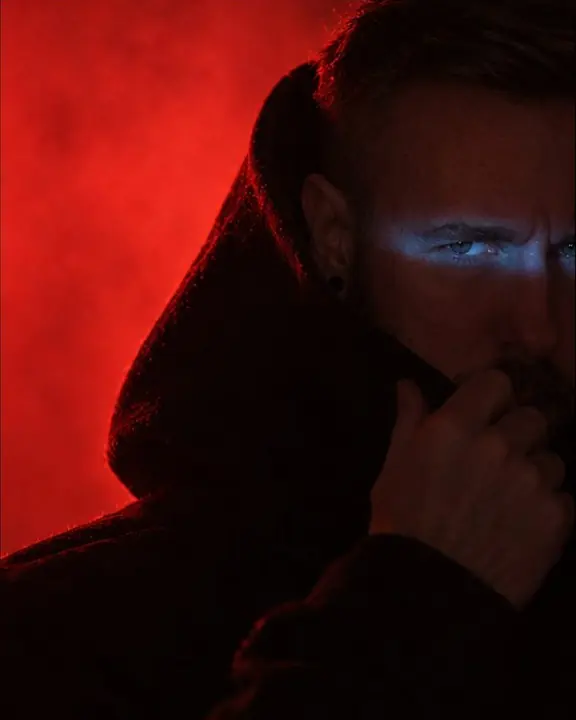 Detail of a black funnel hood edge outlined red by backlit haze, a blue reflection along its rim