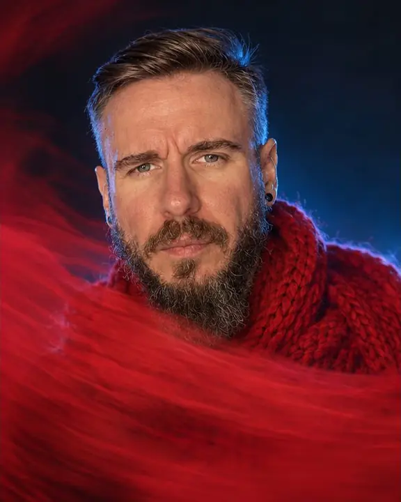 Head and shoulders of a bearded man, his face sharp while a red smear of fabric sweeps across his chest