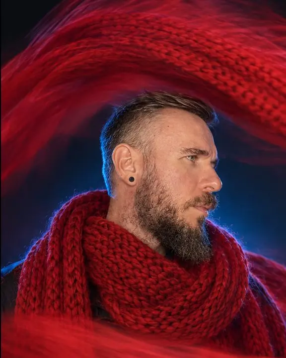 A man in a black boiler suit under a red trail of blurred fabric arching above his head like a wave