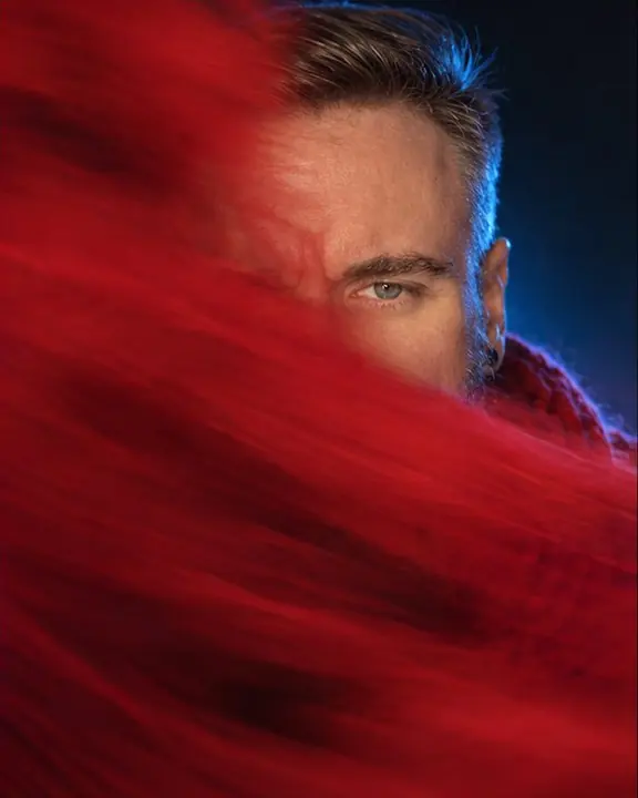 A man half hidden behind a red motion-blurred scarf, one sharp eye visible through the smear