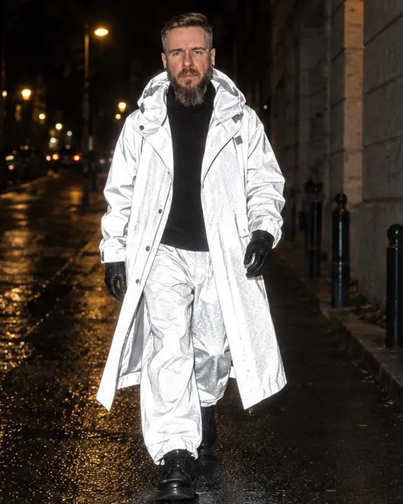 A bearded man walks toward the camera on a dark street, his reflective coat blazing white in the flash