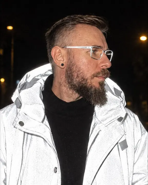Waist-up shot of a man turning his head away, the hood edge and shoulders of his coat burning flash-white