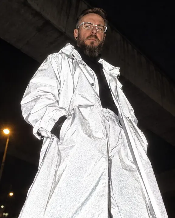 Low angle under a dark overpass: a man's reflective outfit glows as a bright white silhouette against black