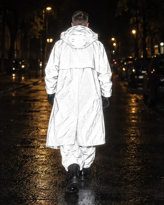 Back view of a man walking away down a night street, his long reflective coat a glowing white shape