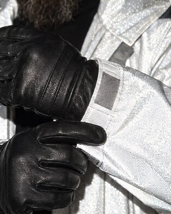 A black leather glove against a retroreflective gray sleeve, tiny glass beads sparkling in the flash