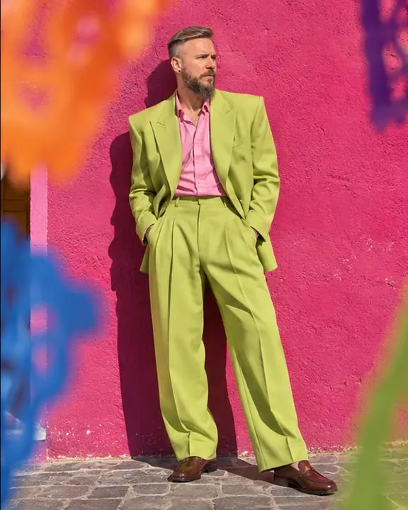 Full-length shot of a man in an acid-green suit against a fuchsia wall, his hard shadow cast beside him