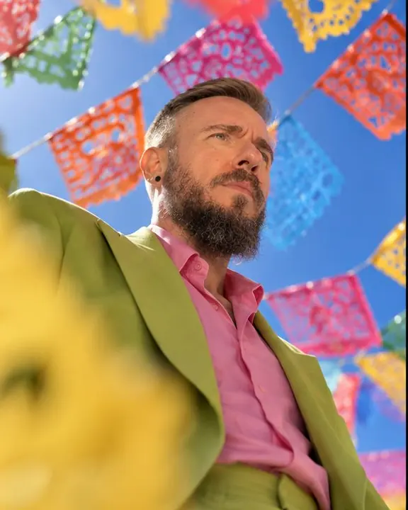 Low angle of a man under strings of colorful papel picado flags against a deep blue sky