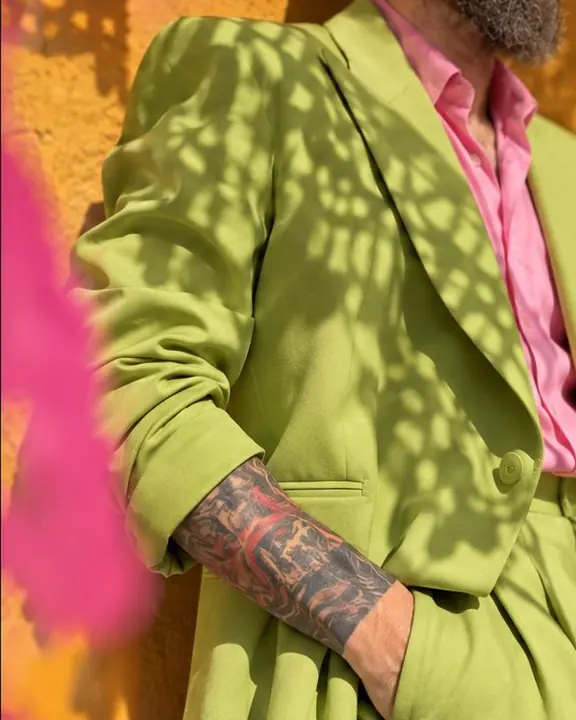 An acid-green suit sleeve covered in lace-like patterned shadow from cut-paper flags in hard sun