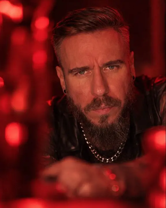 A bearded man looks straight into the lens through a soft red out-of-focus object in the foreground
