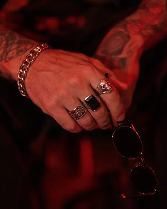 Close-up of hands with chunky silver rings in red light, a cold white LED reflected in the metal