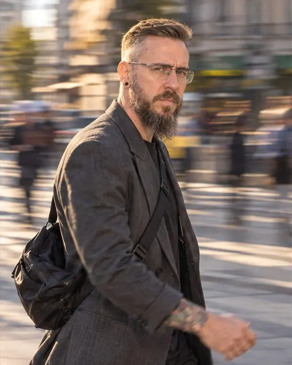 Half-length of a man striding toward the right edge in a charcoal jacket, glancing at the camera, the street blurred