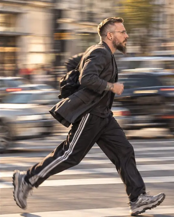 A man runs across a street side-on, his jacket tails flying, the city smeared into streaks behind him