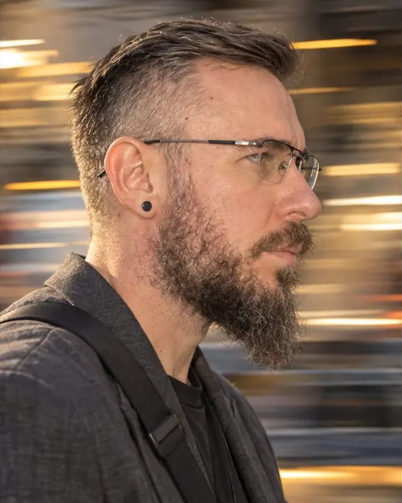 Panning head-and-shoulders profile of a bearded man in sport glasses, face sharp, city lights stretched into lines