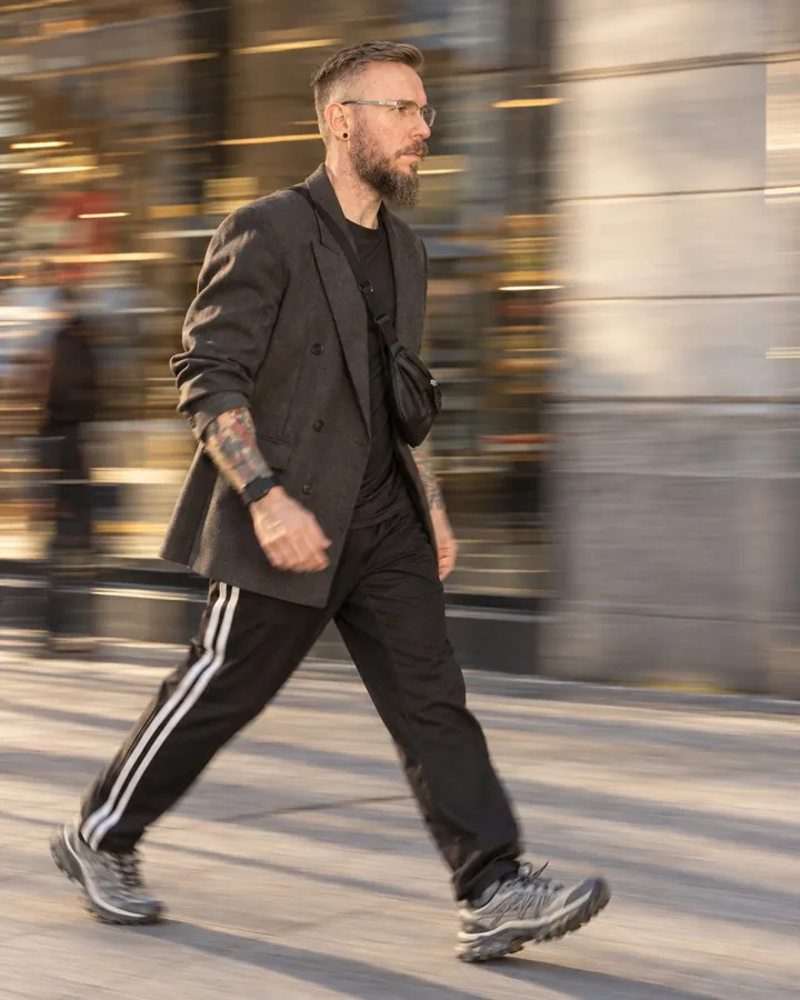 A bearded man walks fast left to right past a shopfront, side-on, the background streaked into horizontal lines