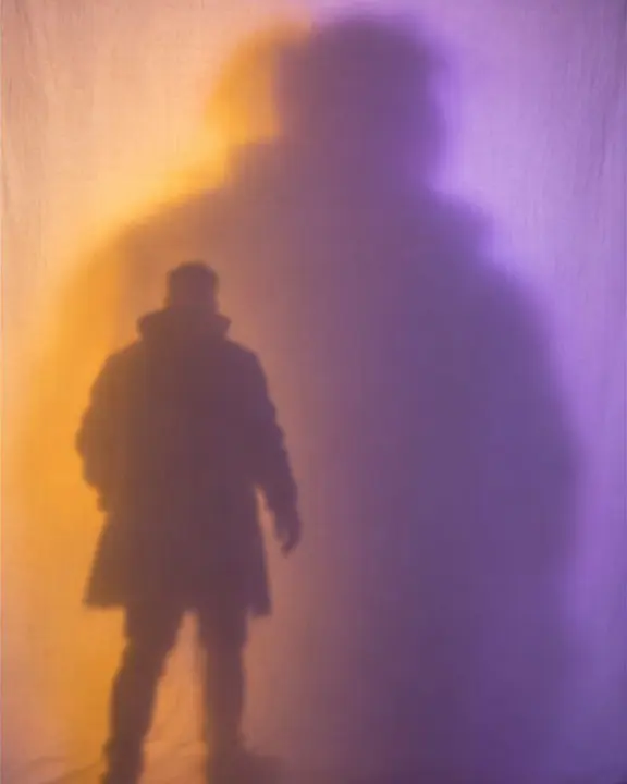 A small sharp shadow of a man overlapping a huge blurred one on a glowing screen as he moves away