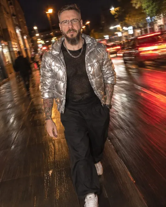 A man walks toward the lens on a night street, red tail-light trails streaking diagonally behind him