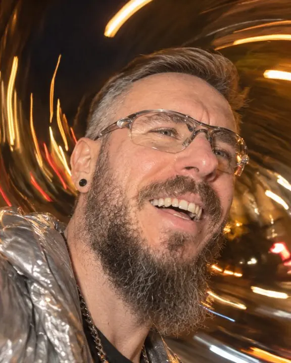 Low-angle close portrait of a bearded man laughing, street lamps spiraling in curved trails around his head