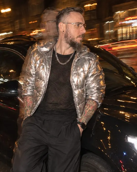 A man leans against a parked car at night, a ghosted double outline of his silhouette offset to the left