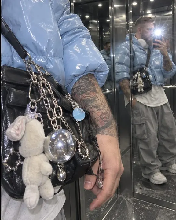 Bag charms and a glossy baby-blue puffer sleeve reflected in an elevator mirror with a bright flash star