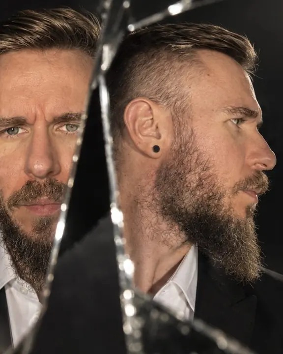 A man's profile in one mirror shard and his frontal face in another, side by side in hard side light