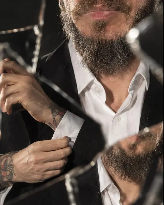 Fragments of a man's hands, white collar and mouth arranged in sharp-edged mirror pieces like a broken portrait