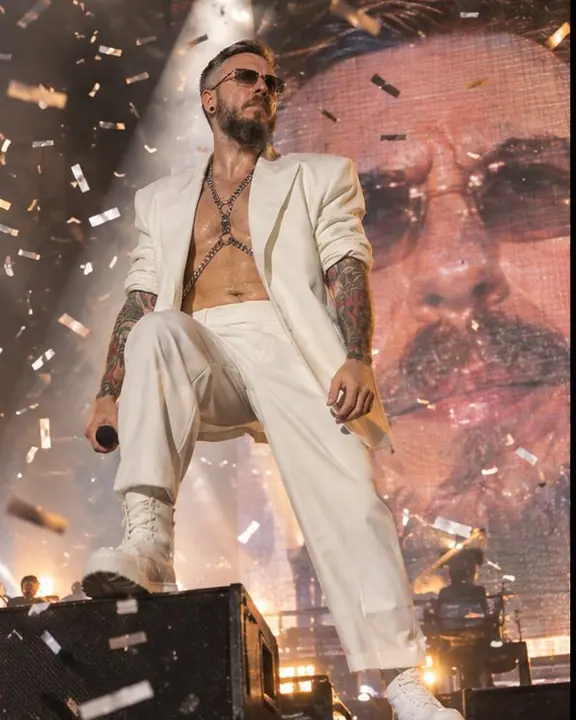 Low-angle shot of a man standing on a riser, confetti in the air, a giant LED close-up of his face behind
