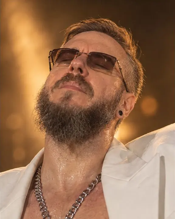 Close portrait of a bearded man with eyes closed, head tilted back into an amber stage beam