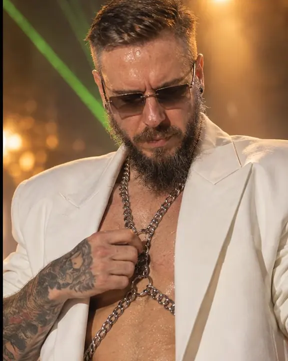 A silver chain harness and a hand against a white stage suit, green laser light reflecting on the metal
