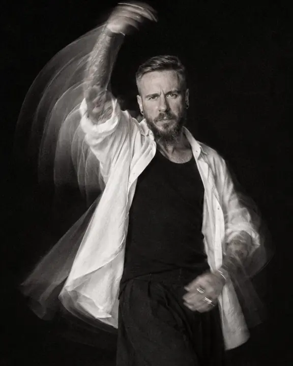 A man swings one arm upward in a fan of blurred arcs, his face turned to the camera and readable