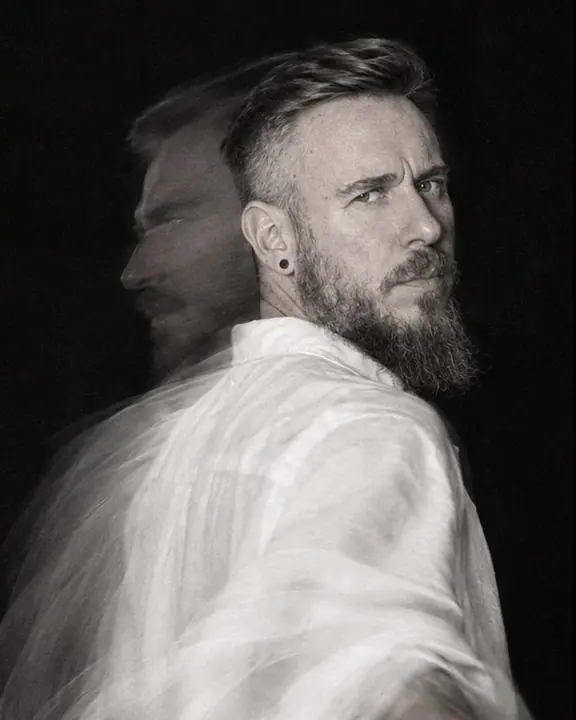 A bearded man turns his head from profile to camera, a double contour of the profile beside his sharp face