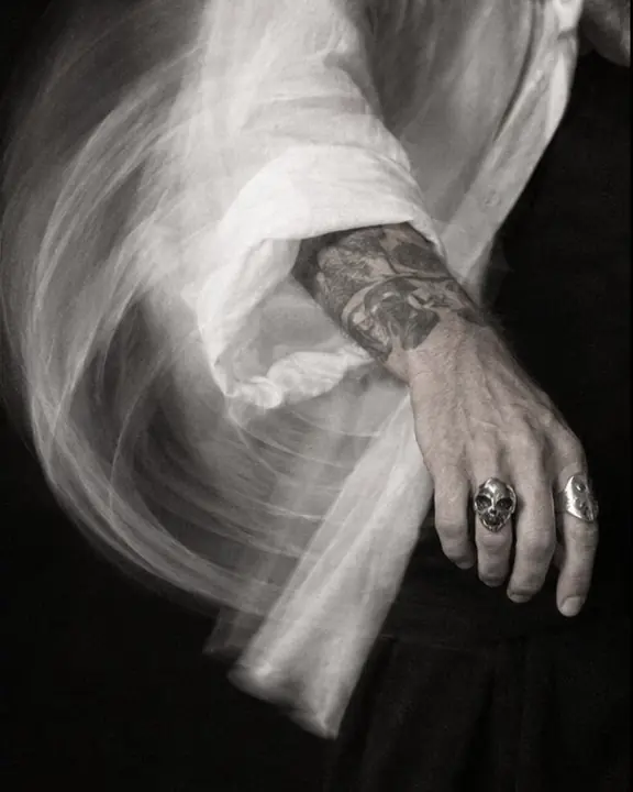A white shirt sleeve and silver-ringed hand drawn into a curved motion trail against a black background