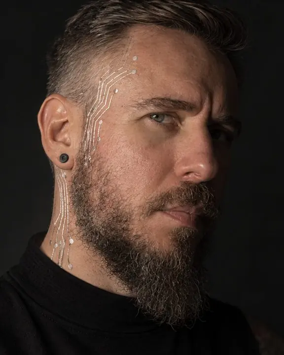 Three-quarter portrait of a man in deep shadow, only the silver lines on his neck and one eye catching light