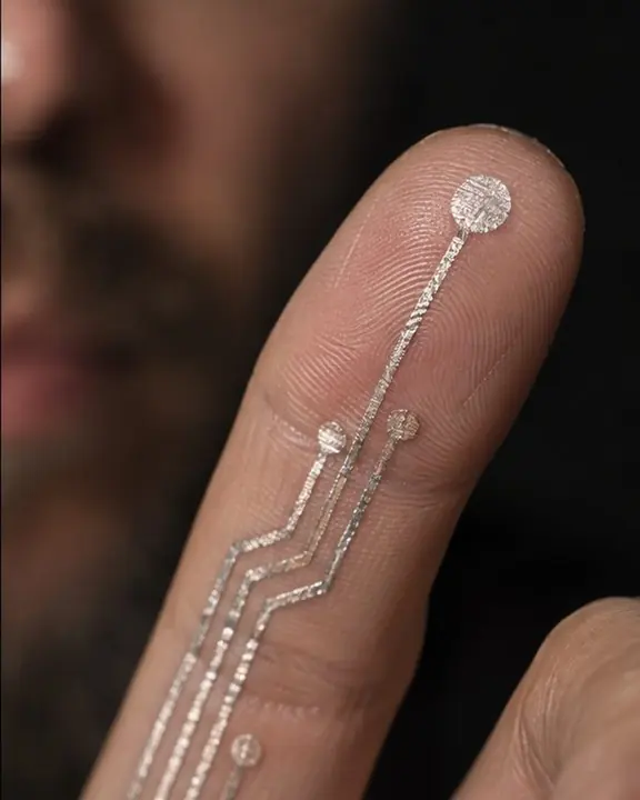Macro of a fingertip with a tiny round sensor dot and thin silver traces printed on the skin