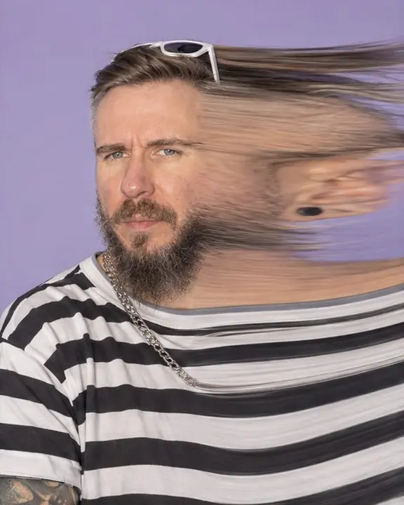A bearded man turns his head during a slit scan, one side of his face stretched into a ribbon, both eyes sharp