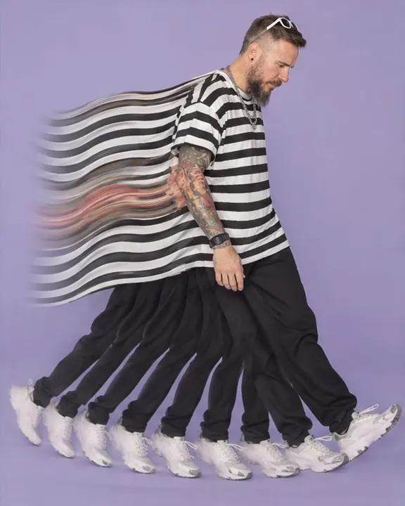 A man stepping in place, his legs multiplied into a fan of black-and-white stripes against a lilac backdrop