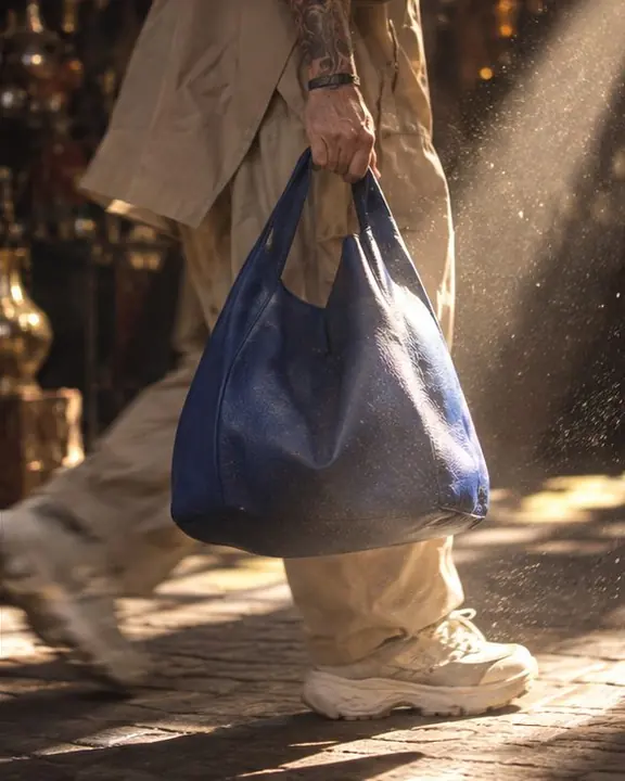 A cobalt leather bag caught in a narrow sunbeam with dust glowing in the air around it