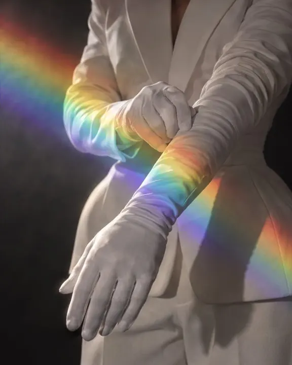 Detail of a white opera glove lit by a band of rainbow light from a prism, black all around it