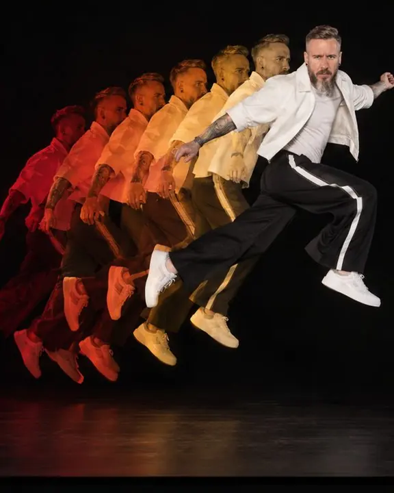 A bearded man jumps left to right in seven colored phases from red to white, the white peak phase facing the camera