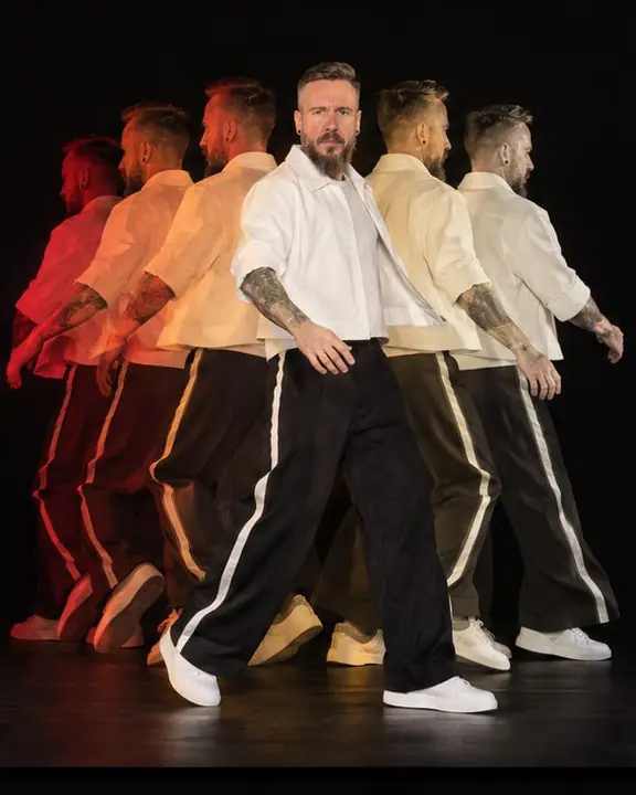 A man spins in place in six overlapping colored phases on black, the final white phase facing the lens