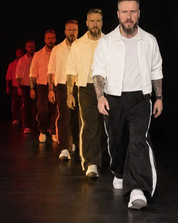 A bearded man walks toward the camera in phases growing larger, from red at the back to sharp white in front