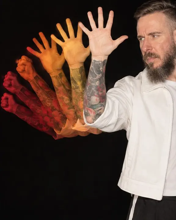 A single hand opening in seven overlapping phases, each one lit a different color from red to white