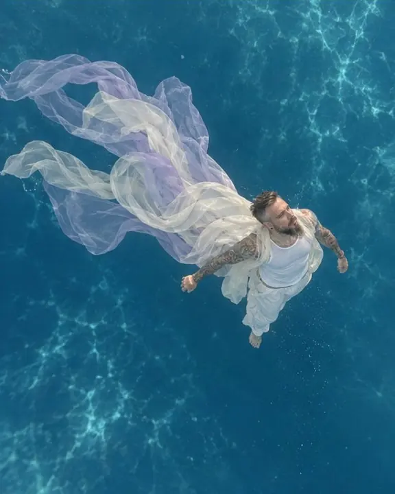 High-angle view into blue depth, a small figure in white below with ivory fabric trailing behind